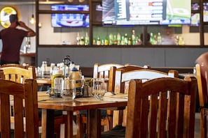 Un restaurante con mesas y sillas de madera, una zona de bar con botellas y varias pantallas mostrando contenido deportivo.