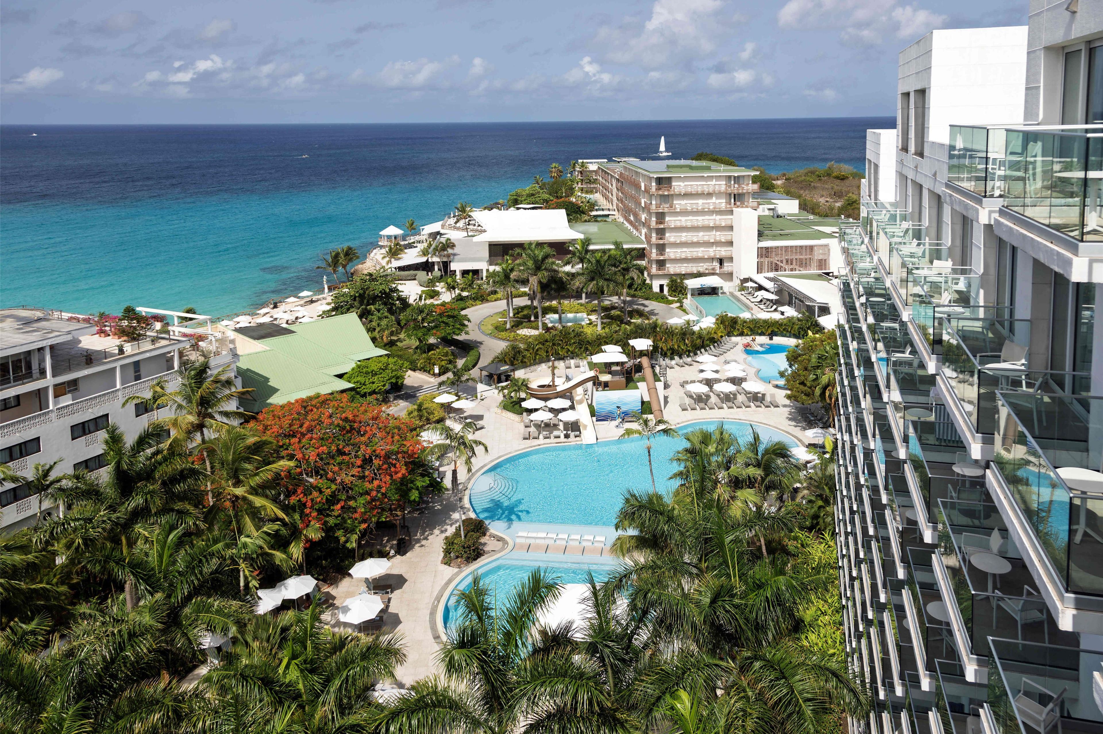 A resort with a large pool, palm trees, and a view of the ocean.