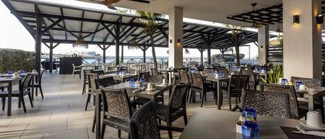 Un espace extérieur aménagé pour les repas, avec des tables et des chaises, un toit abrité et une vue sur la mer.