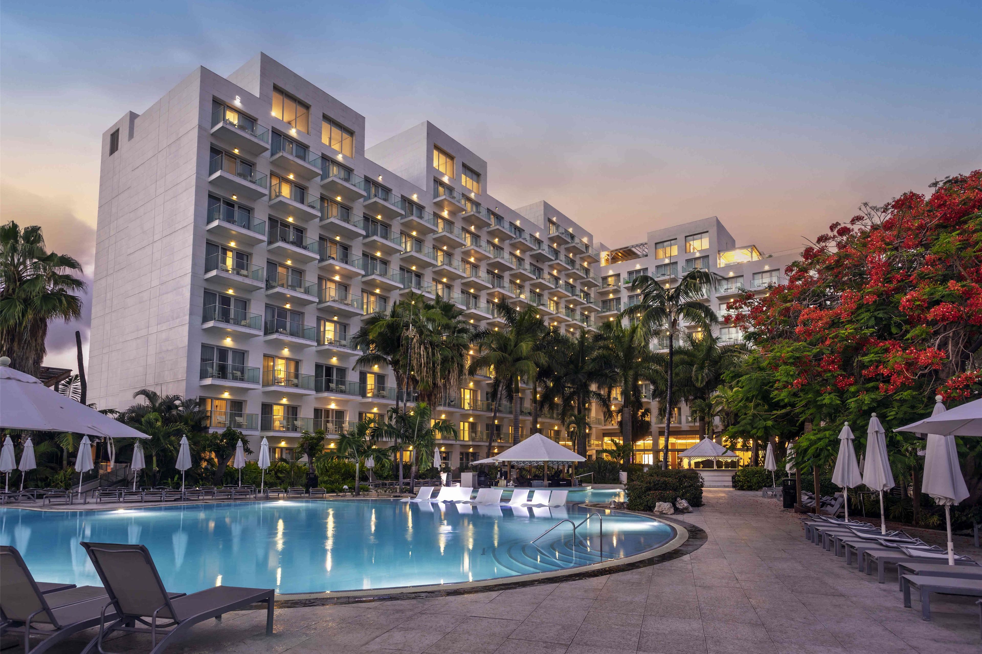 Un hotel con una piscina grande, varios balcones y palmeras.