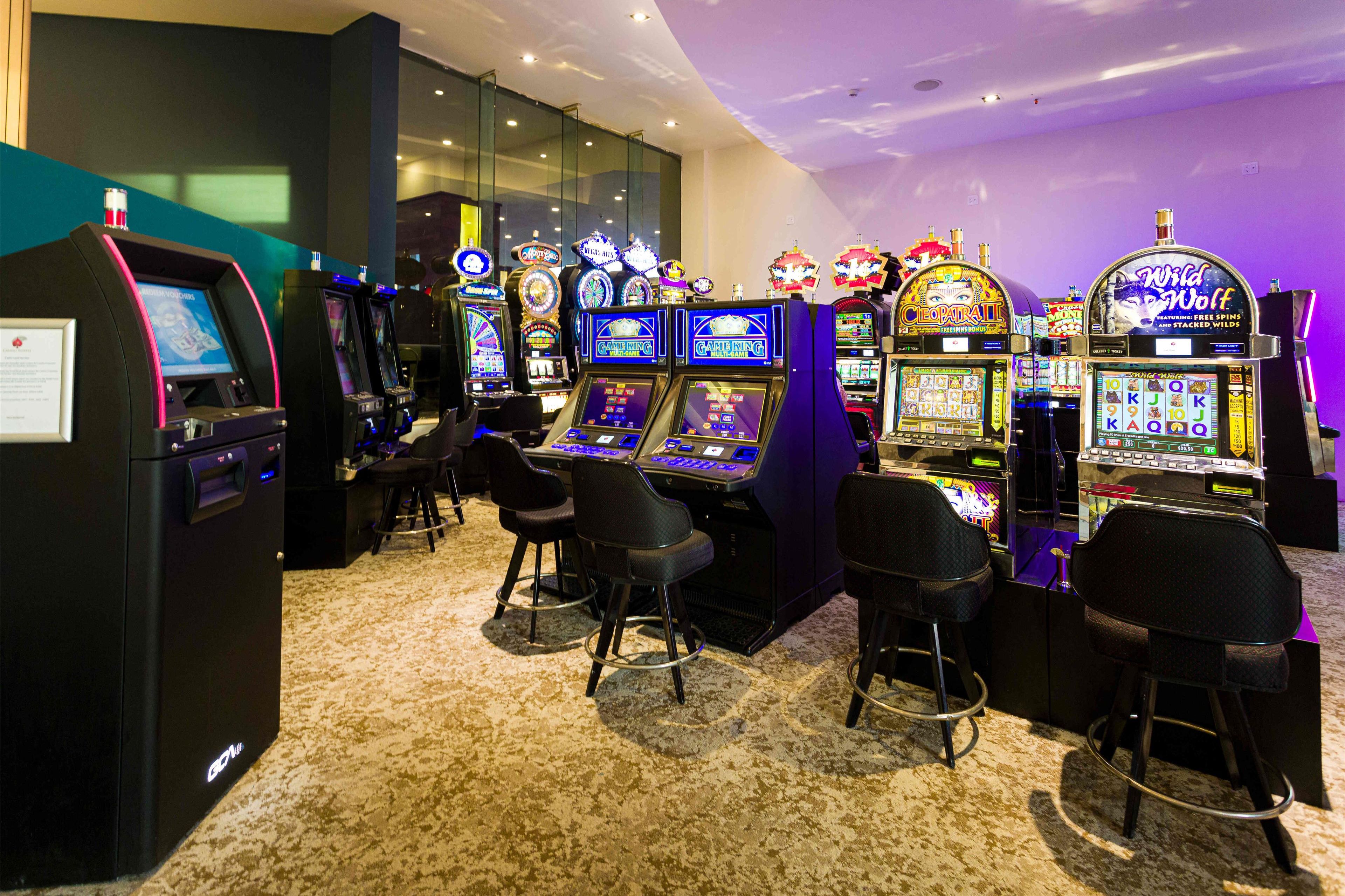 A casino with multiple slot machines and bar stools.