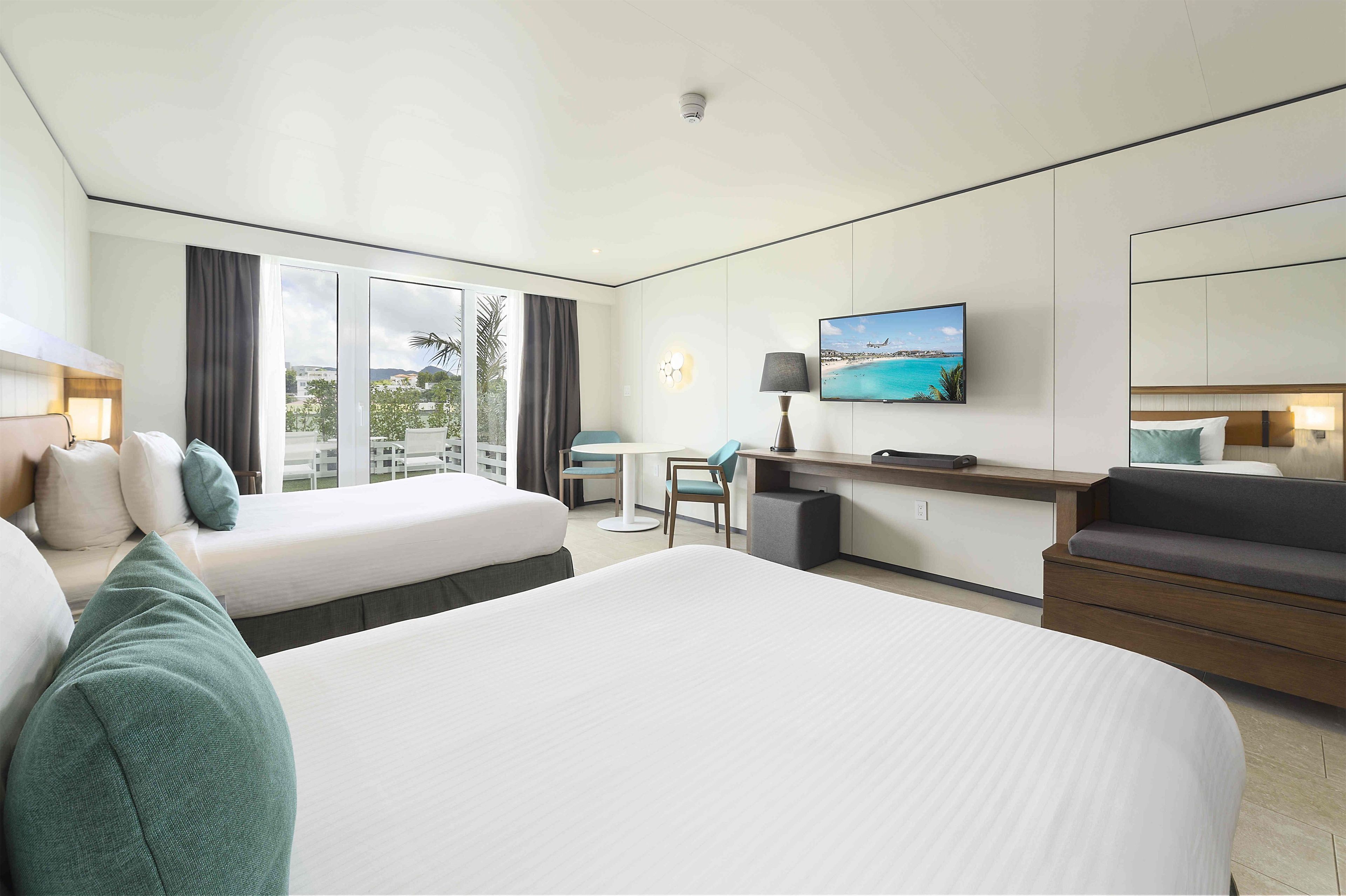 A hotel room with two beds, a desk, a TV, and a view of the outdoors.