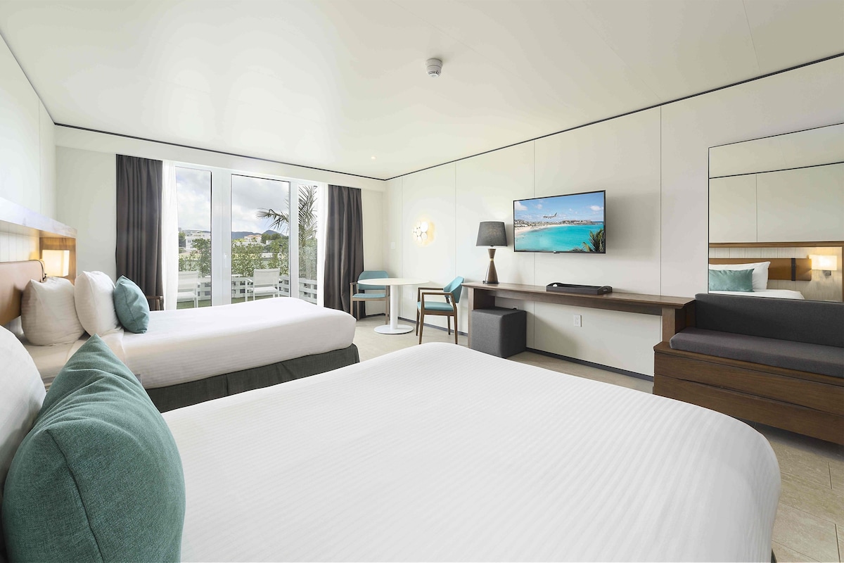 Ein Hotelzimmer mit zwei Betten, einem Schreibtisch, einem Fernseher und Blick ins Freie.