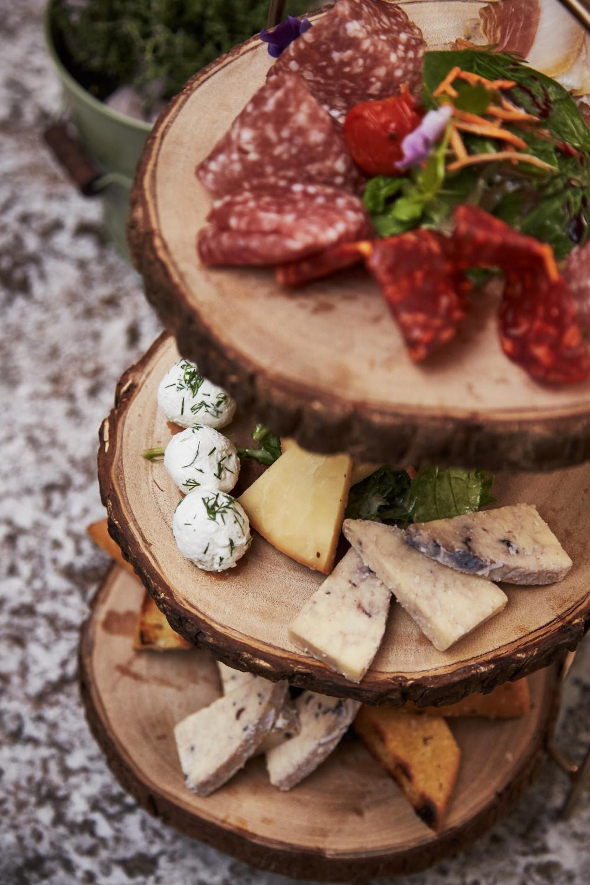 A multi-tiered wooden board with various cheeses, cured meats, and a small salad.