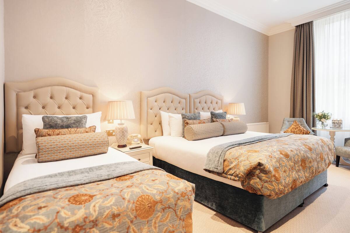 A hotel room with two beds, a sitting area, and a view of the outdoors.