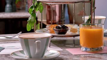 A three-tiered metal stand with pastries, fruits, and beverages on a table.