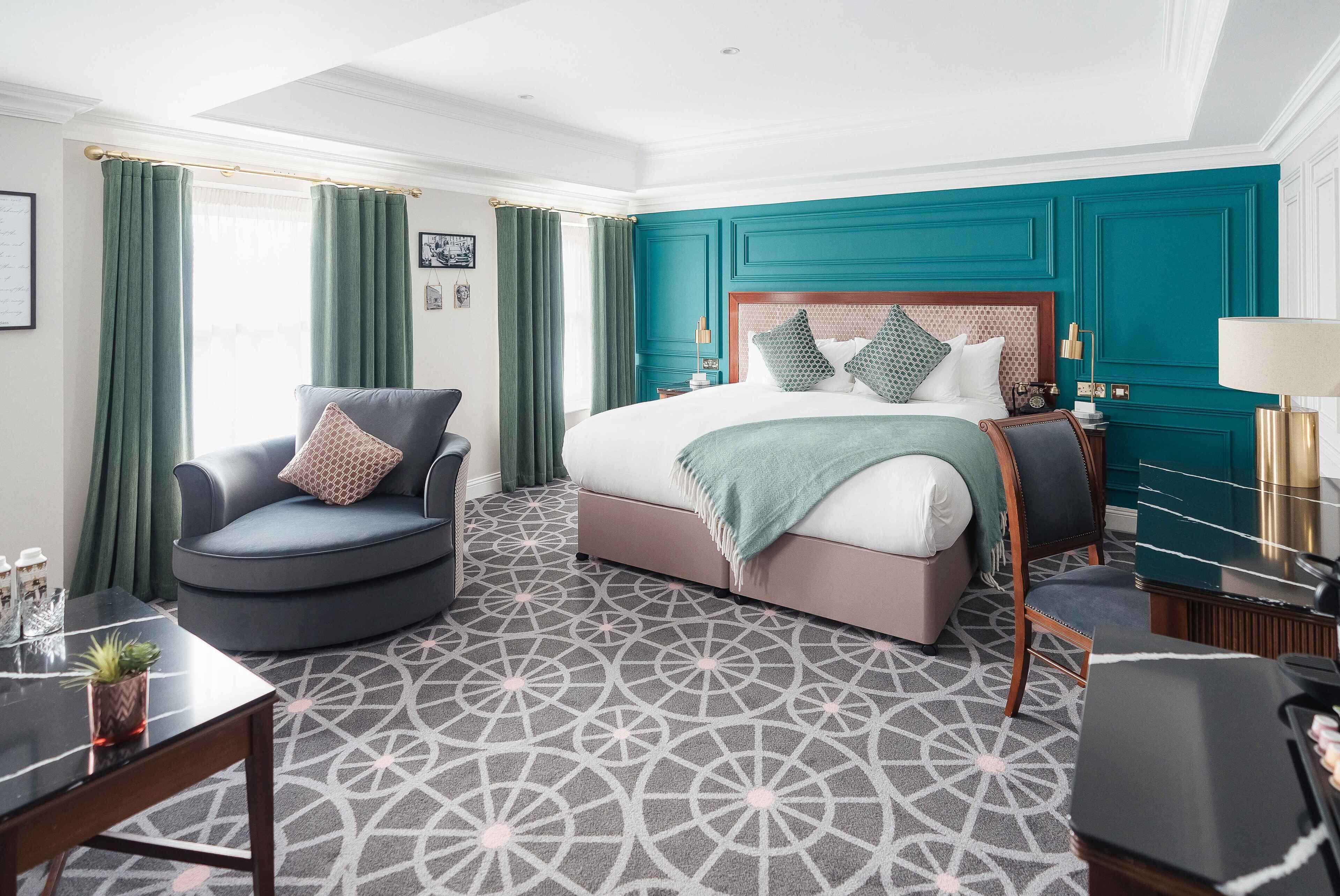 A hotel room with a large bed, a curved armchair, a small table, and a desk.