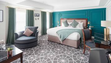A hotel room with a large bed, a curved armchair, a small table, and a desk.