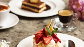 A dessert plate with a meringue topped with strawberries and mint, a coffee cup, and a slice of cake on a marble table.