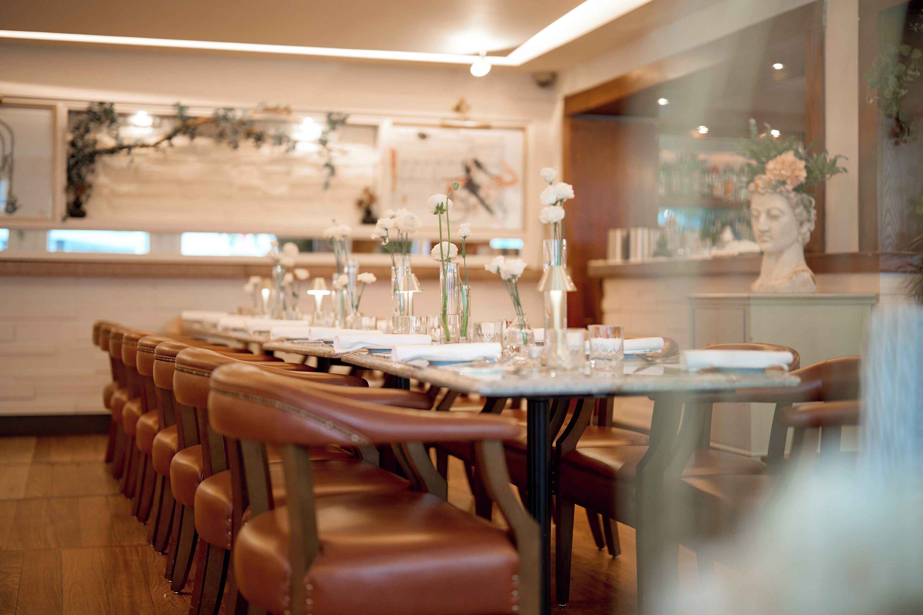 Un restaurant avec une longue table dressée pour le repas, des chaises en bois et un buste décoratif accroché au mur.