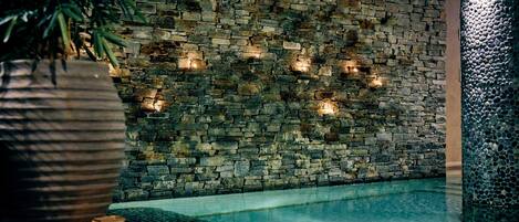Un muro de piedra con luces empotradas, una piscina y una planta grande en maceta.