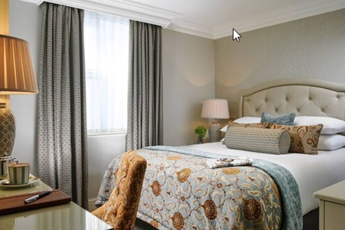 A hotel room with a bed, a chair, a table, and a lamp.