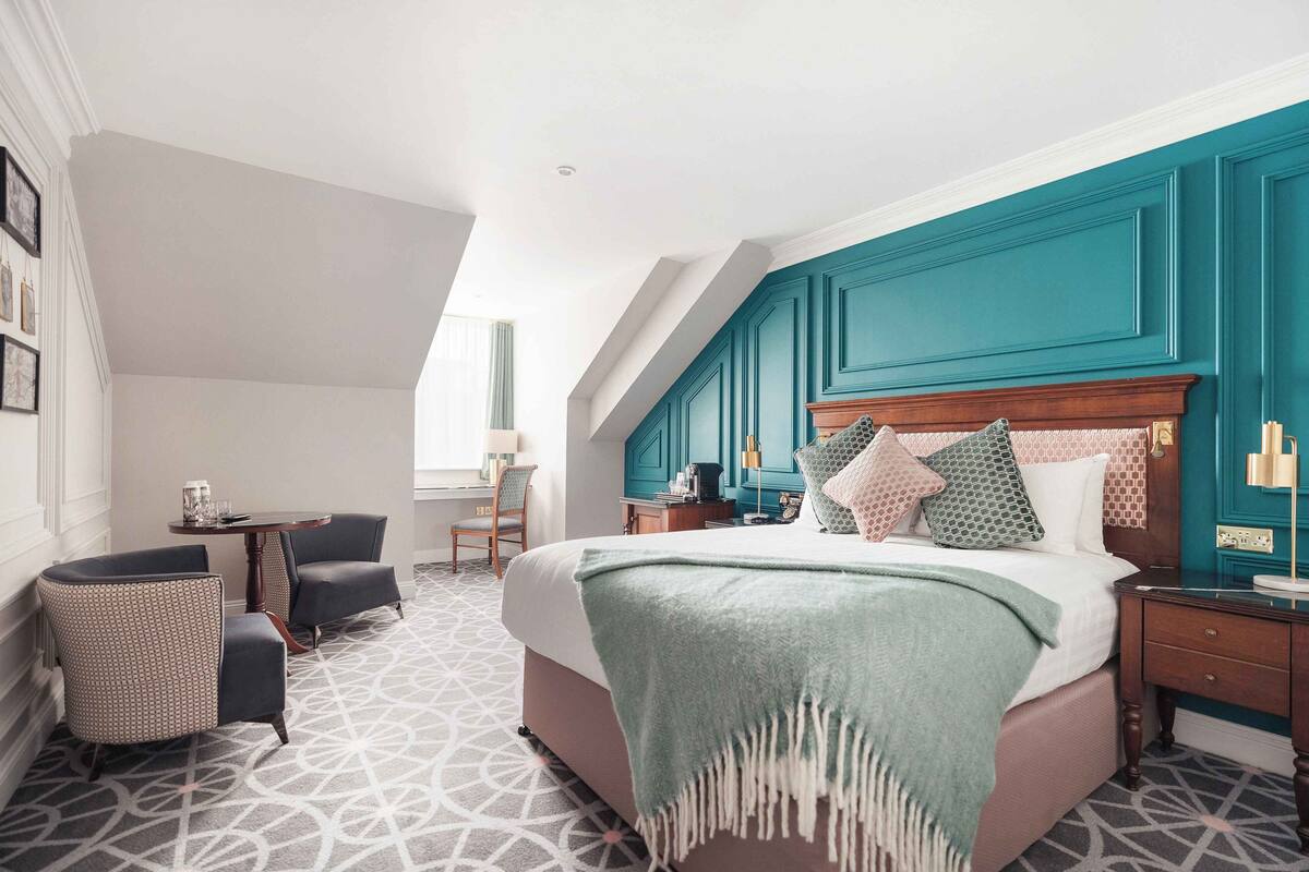 A bedroom with a large bed, a desk, a chair, and a window.