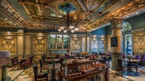An ornate restaurant interior with a central wooden table displaying pastries and bread, surrounded by chairs and tables. - Imperial Hotel (Cork)