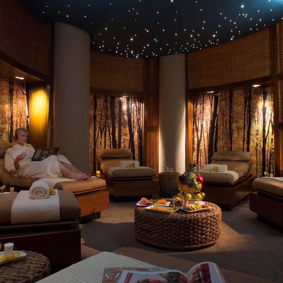 A spa room with two reclining chairs, a small table with fruits and a glass of water, and a starry ceiling.