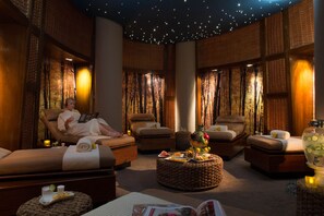 Un cuarto de spa con dos sillones reclinables, una mesita con frutas y un vaso de agua, y un techo estrellado.