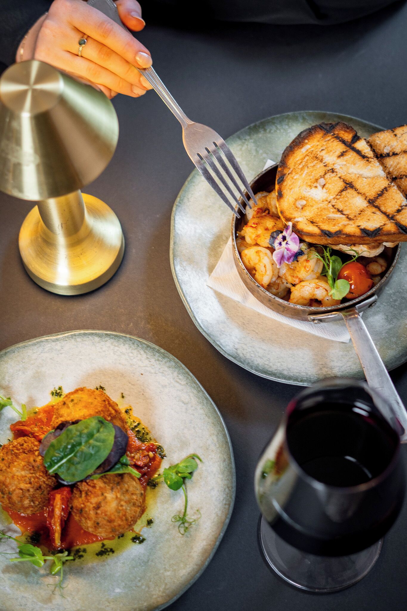 A dining table with plates of food, a wine glass, and a metal pitcher.