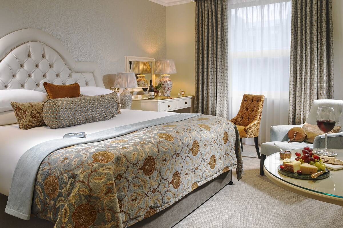 A luxurious bedroom with a large bed, a sitting area with a glass table, and a view through curtains.