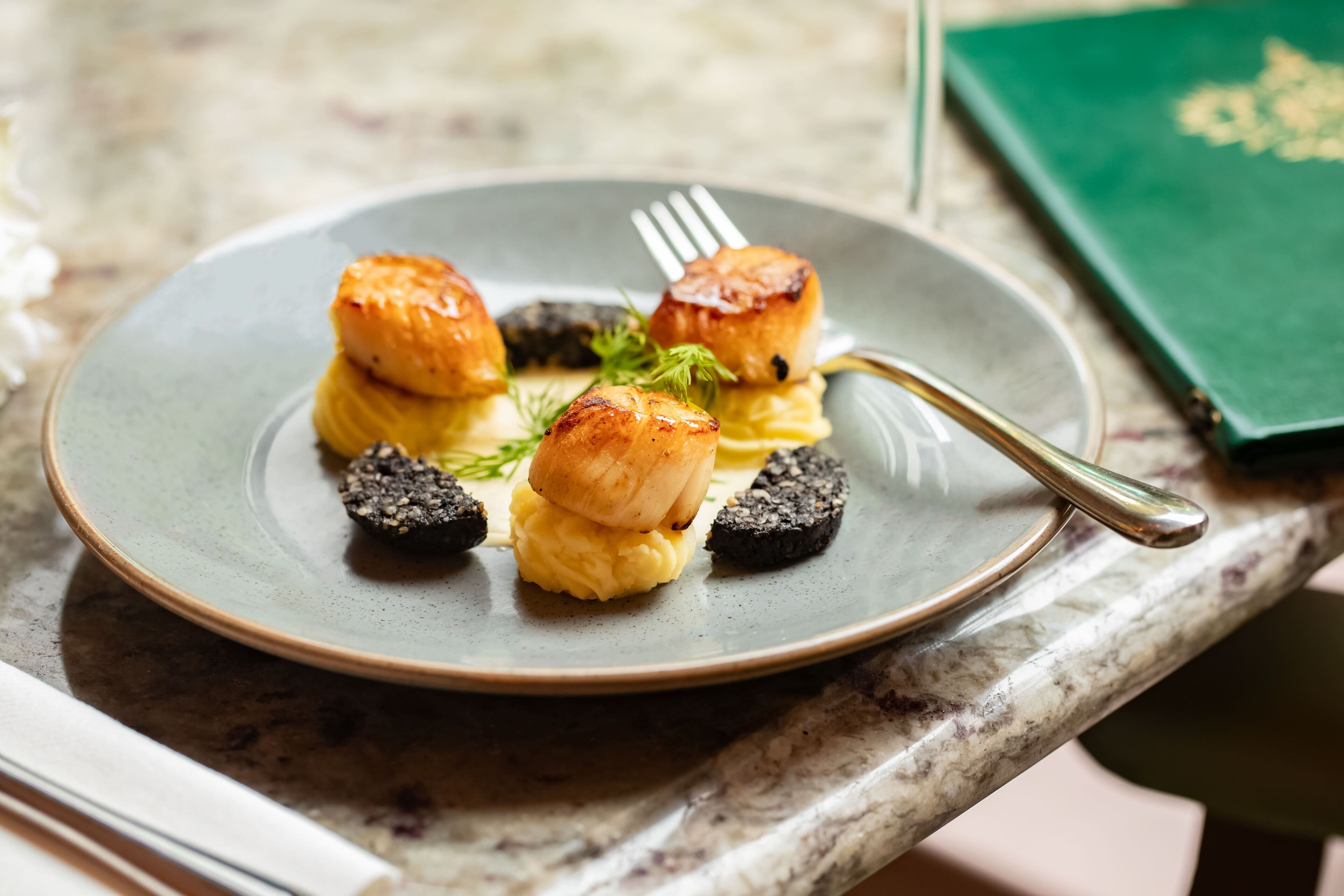 Een bord met coquilles en puree op een marmeren blad.