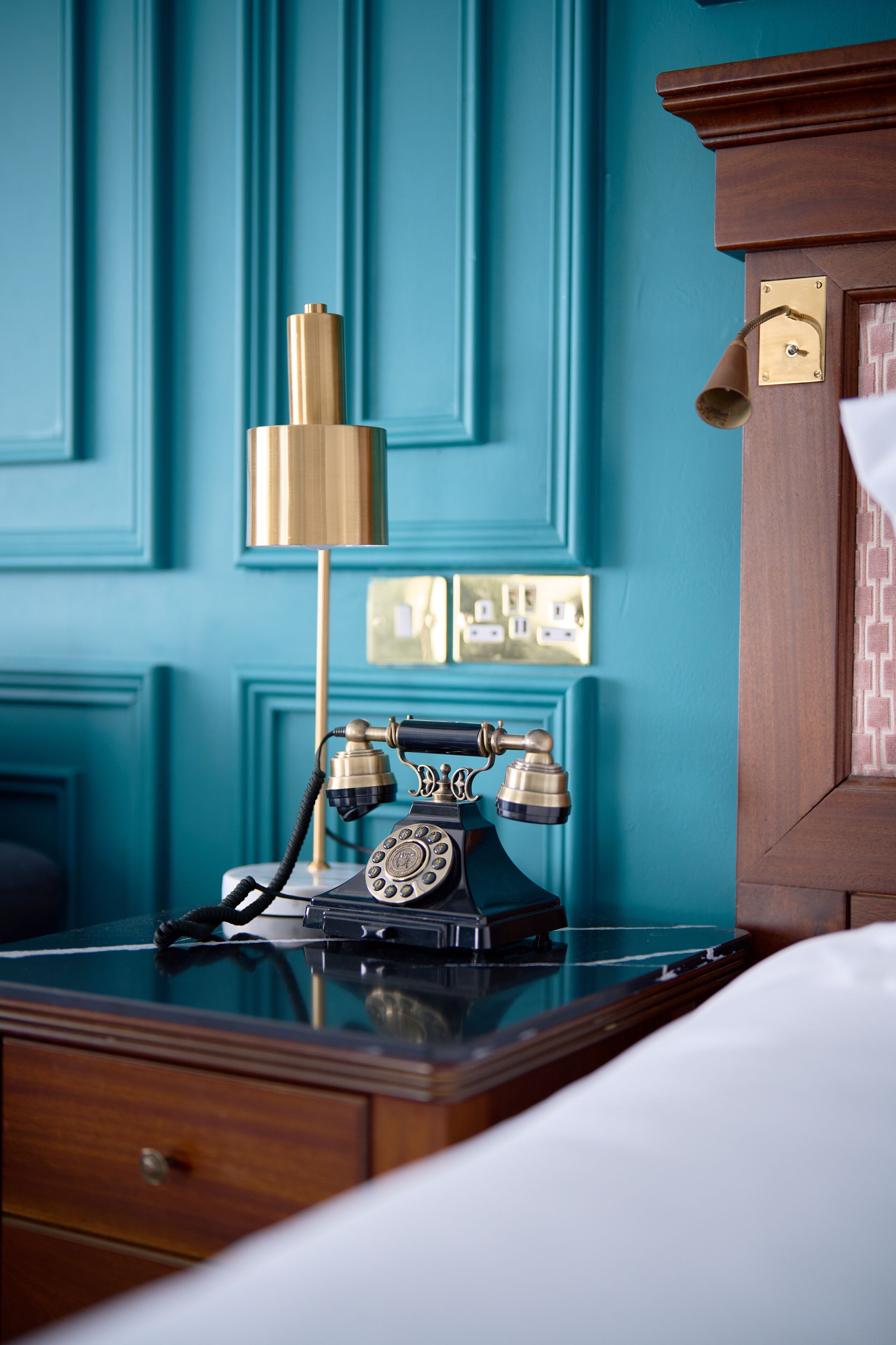 A vintage telephone on a wooden desk with a teal wall in the background.