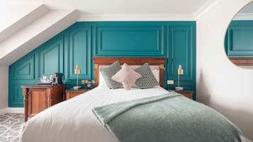Un dormitorio con paredes color turquesa, un cabecero de madera, una cama con sábanas blancas, dos mesitas de noche con lámparas y una alfombra estampada.