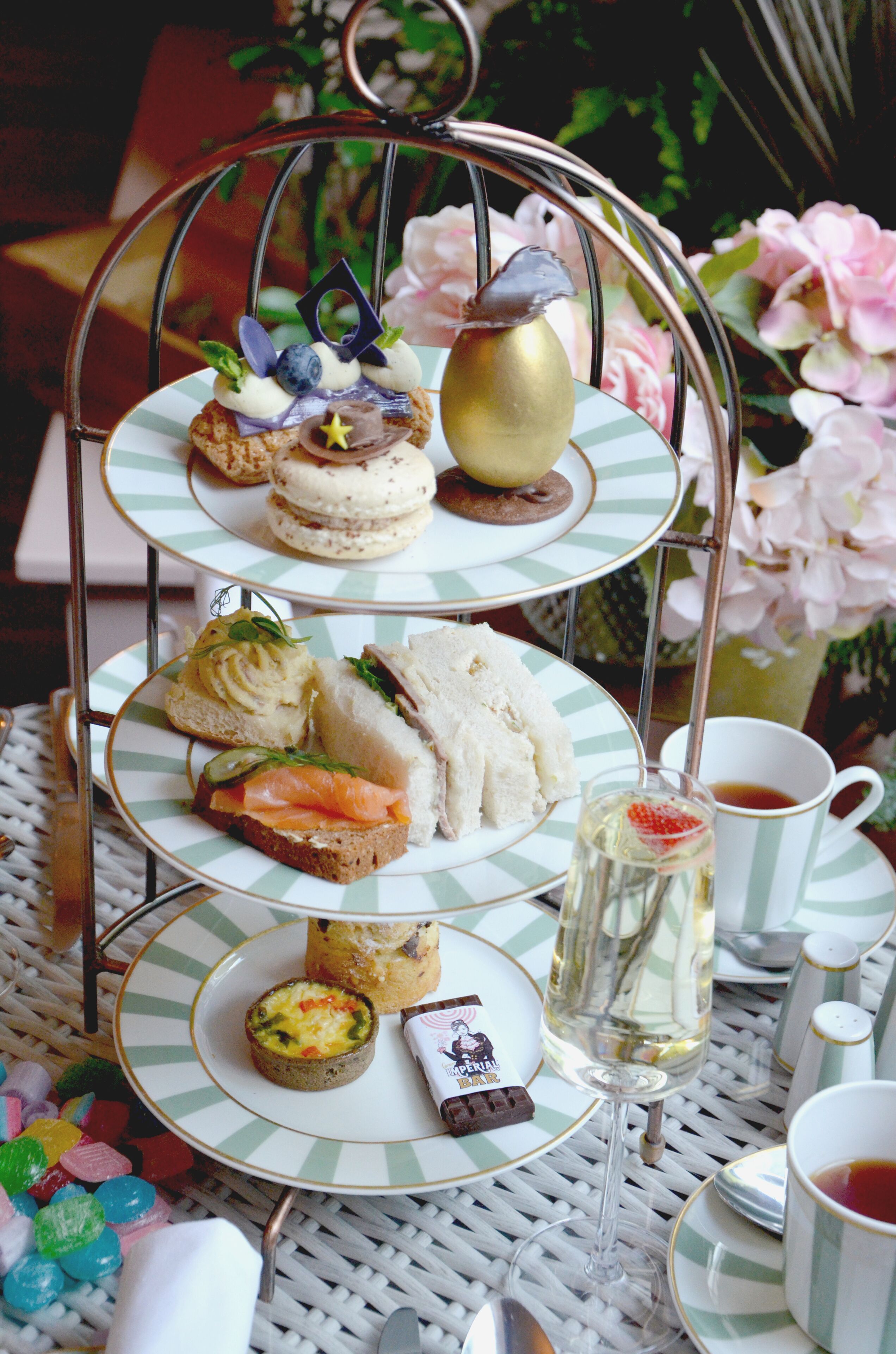 A three-tiered stand with various sandwiches and desserts, a glass of champagne, and a cup of tea.