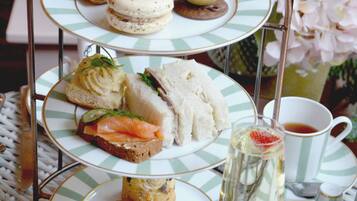 A three-tiered stand with various sandwiches and desserts, a glass of champagne, and a cup of tea.