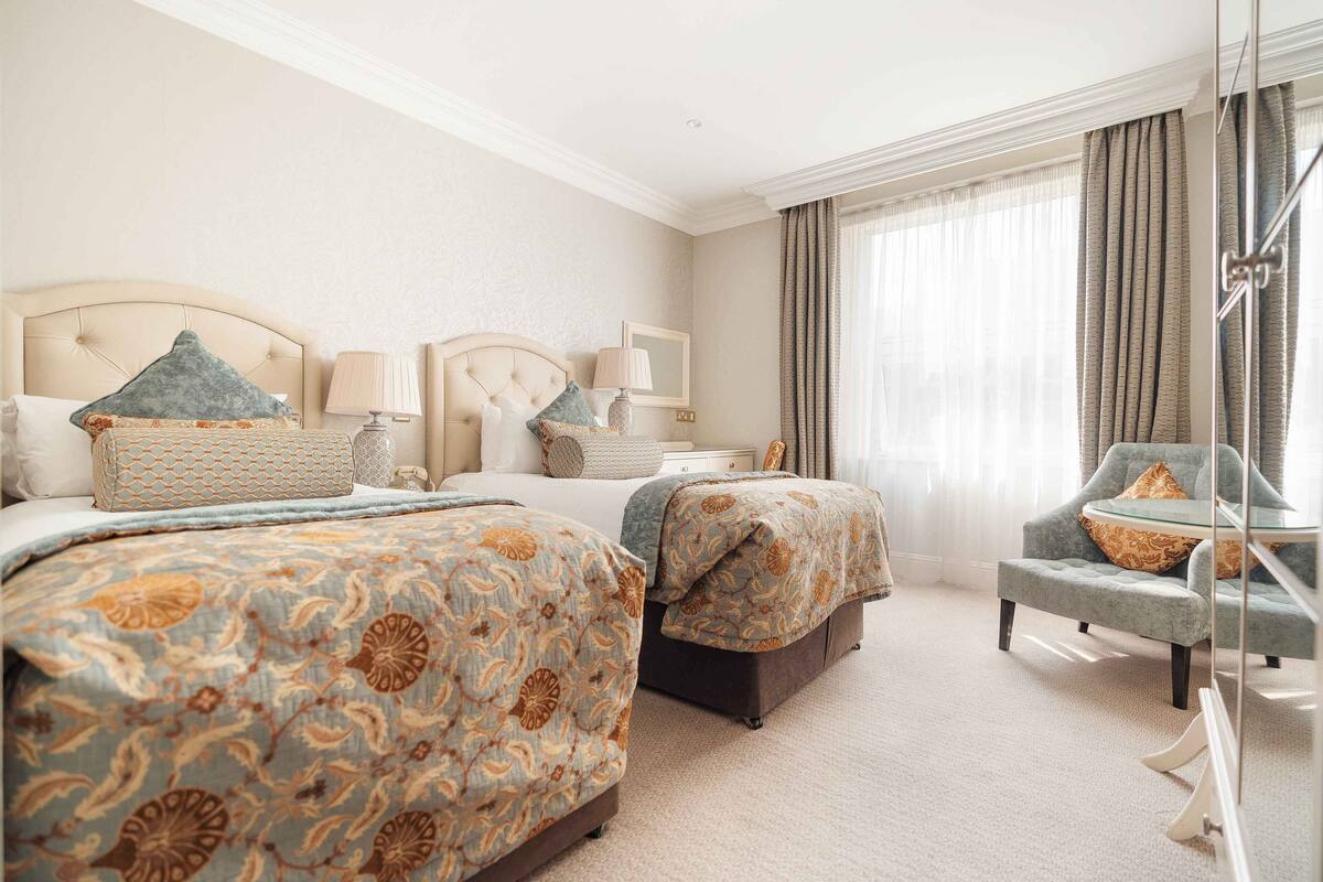 A hotel room with two beds, a sitting area, and a large window with curtains.