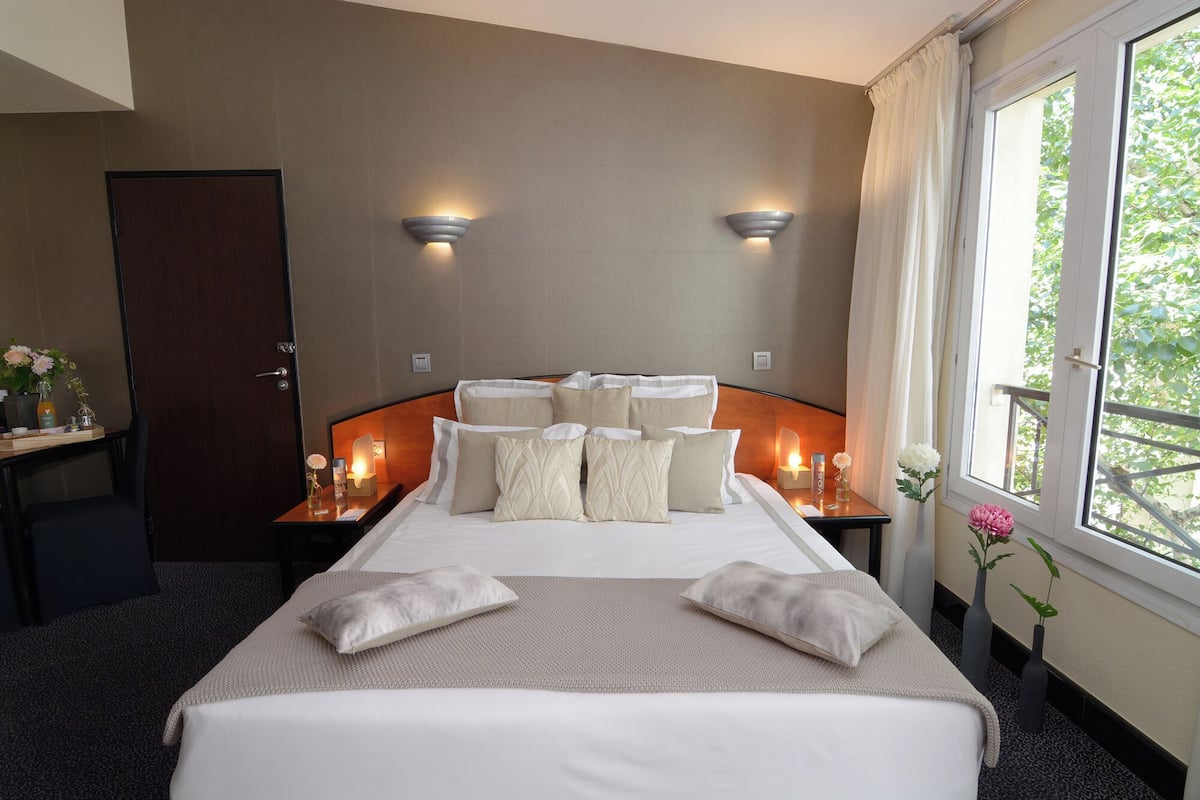 Quarto de hotel com uma cama grande, duas mesas de cabeceira, uma escrivaninha e uma janela com cortinas.