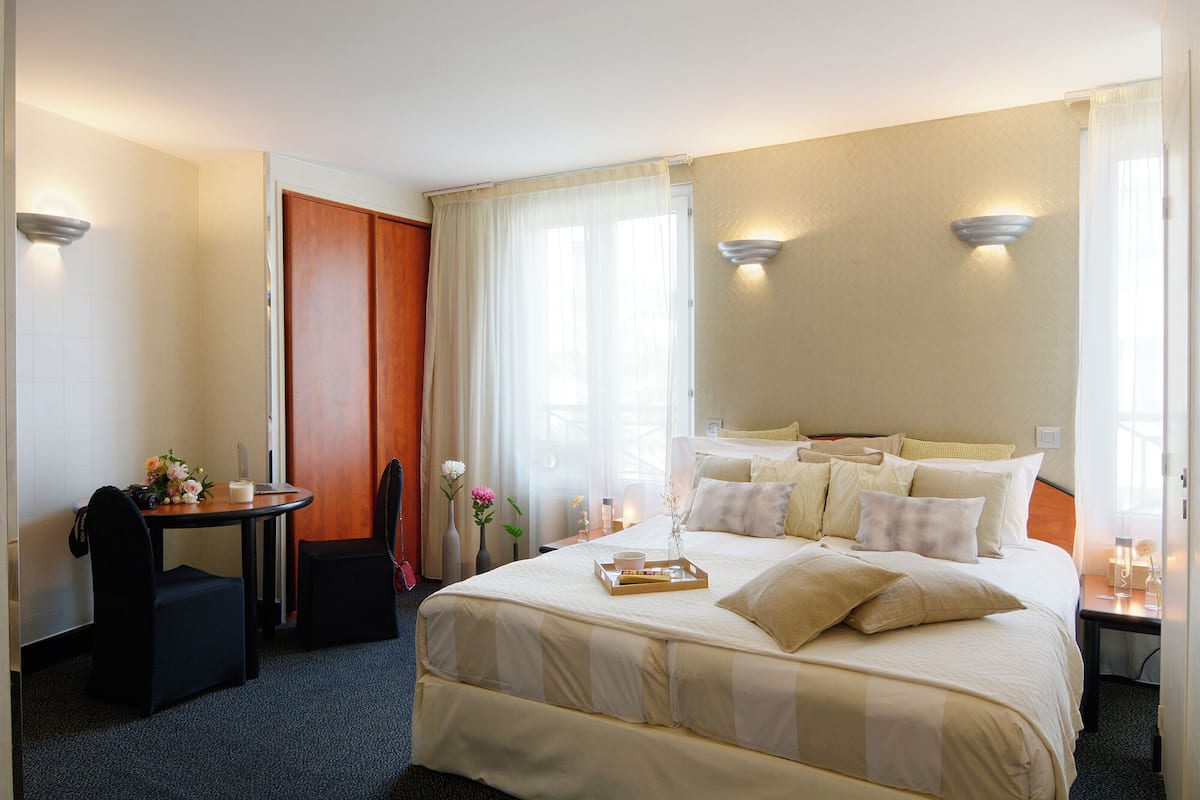Quarto de hotel com uma cama grande, uma pequena mesa, uma cadeira e uma escrivaninha.