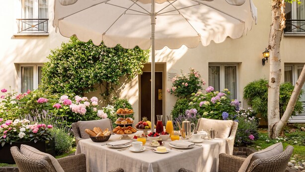 An outdoor dining area with wicker chairs, a table set with breakfast, and a large umbrella. - Le patio Bastille (Paris)