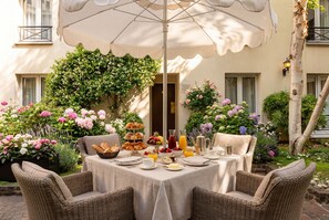 An outdoor dining area with wicker chairs, a table set with breakfast, and a large umbrella. - Le patio Bastille (Paris)