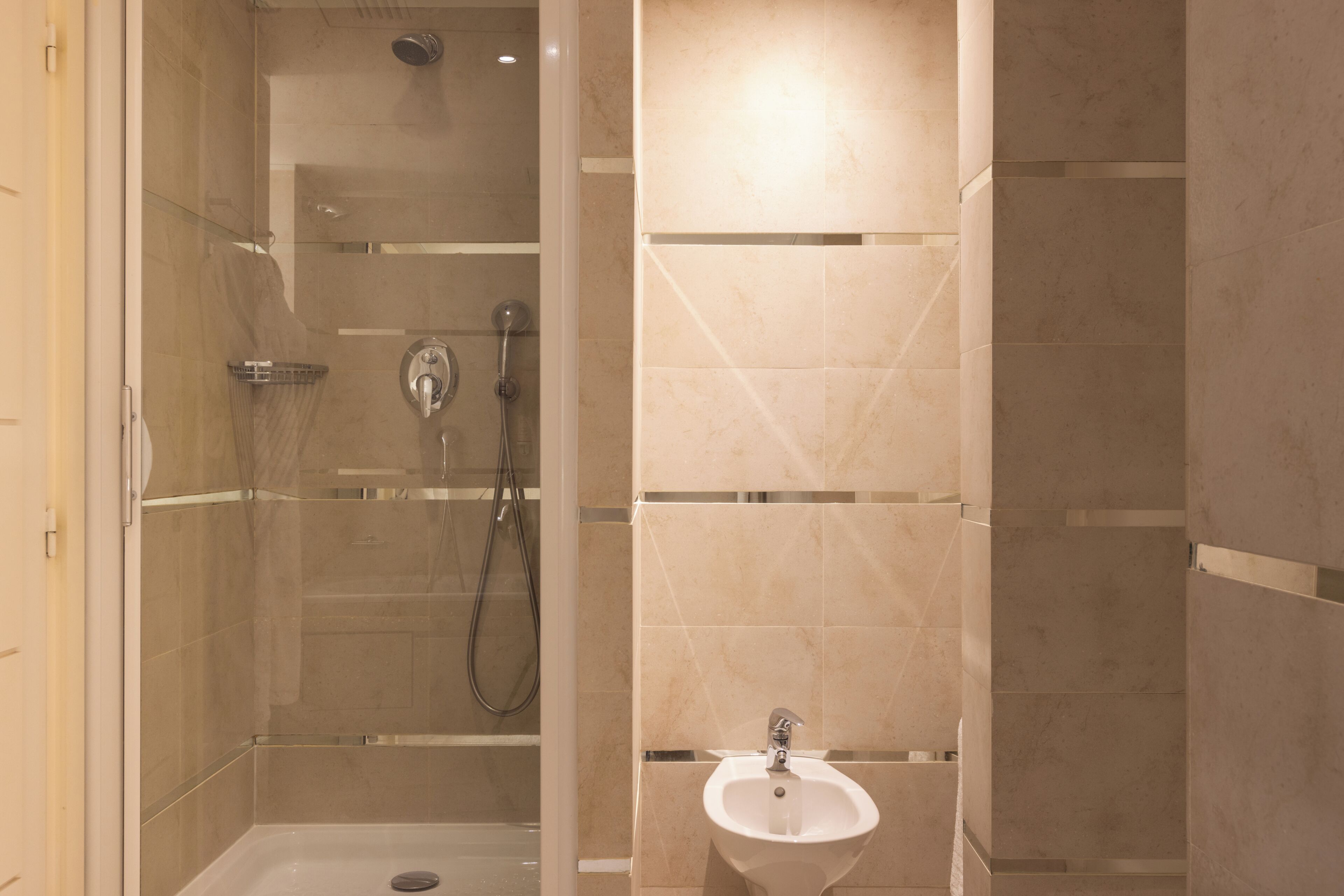 A bathroom with a glass-enclosed shower, a sink, and tiled walls.