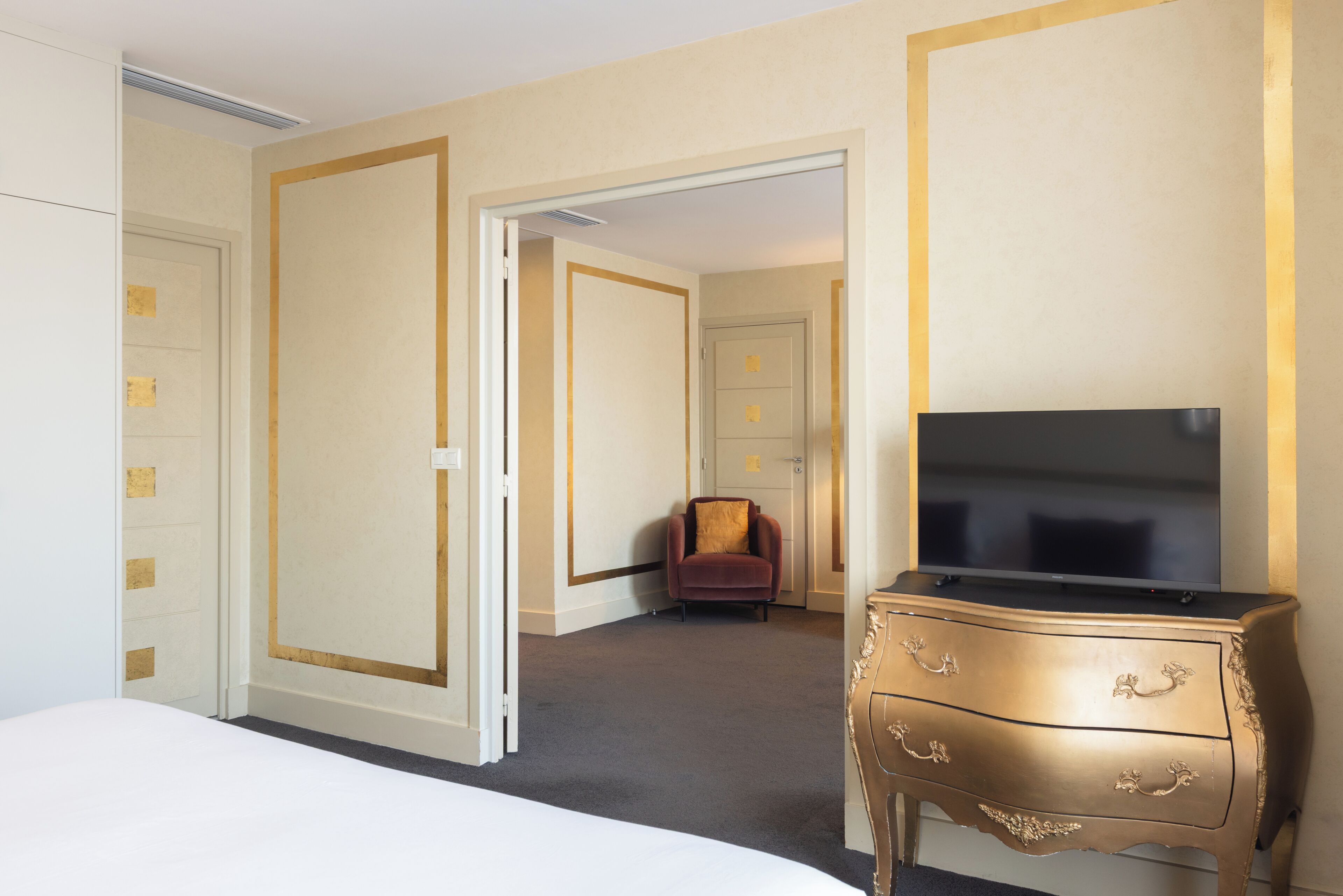 A hotel room with a bed, a TV on a dresser, and a chair in the corner.