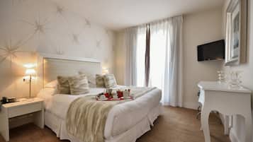 Una habitación de hotel ordenada con una cama grande, lámparas de noche, un escritorio y un televisor montado en la pared.