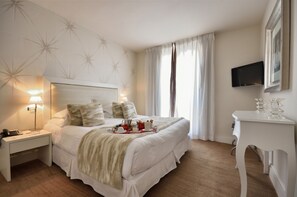 A neatly arranged hotel room with a large bed, bedside lamps, a desk, and a TV mounted on the wall. - Hotel Renoir (Cannes)