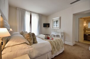 Habitación de hotel con una cama grande, una mesita de noche, un televisor y un baño visible a través de una puerta abierta.