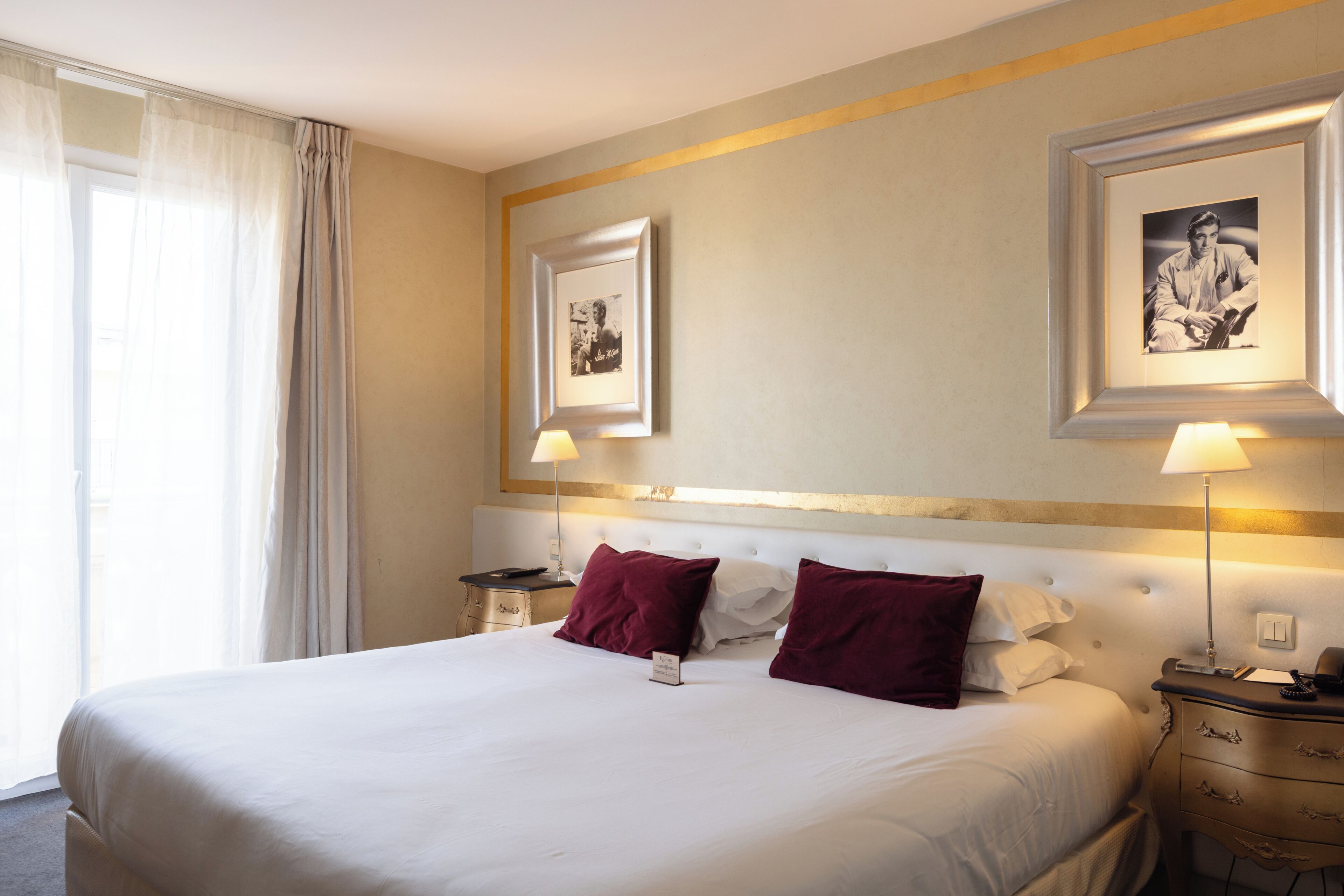 A hotel room with a large bed, two bedside tables, a nightstand, a lamp, and two framed pictures on the wall.