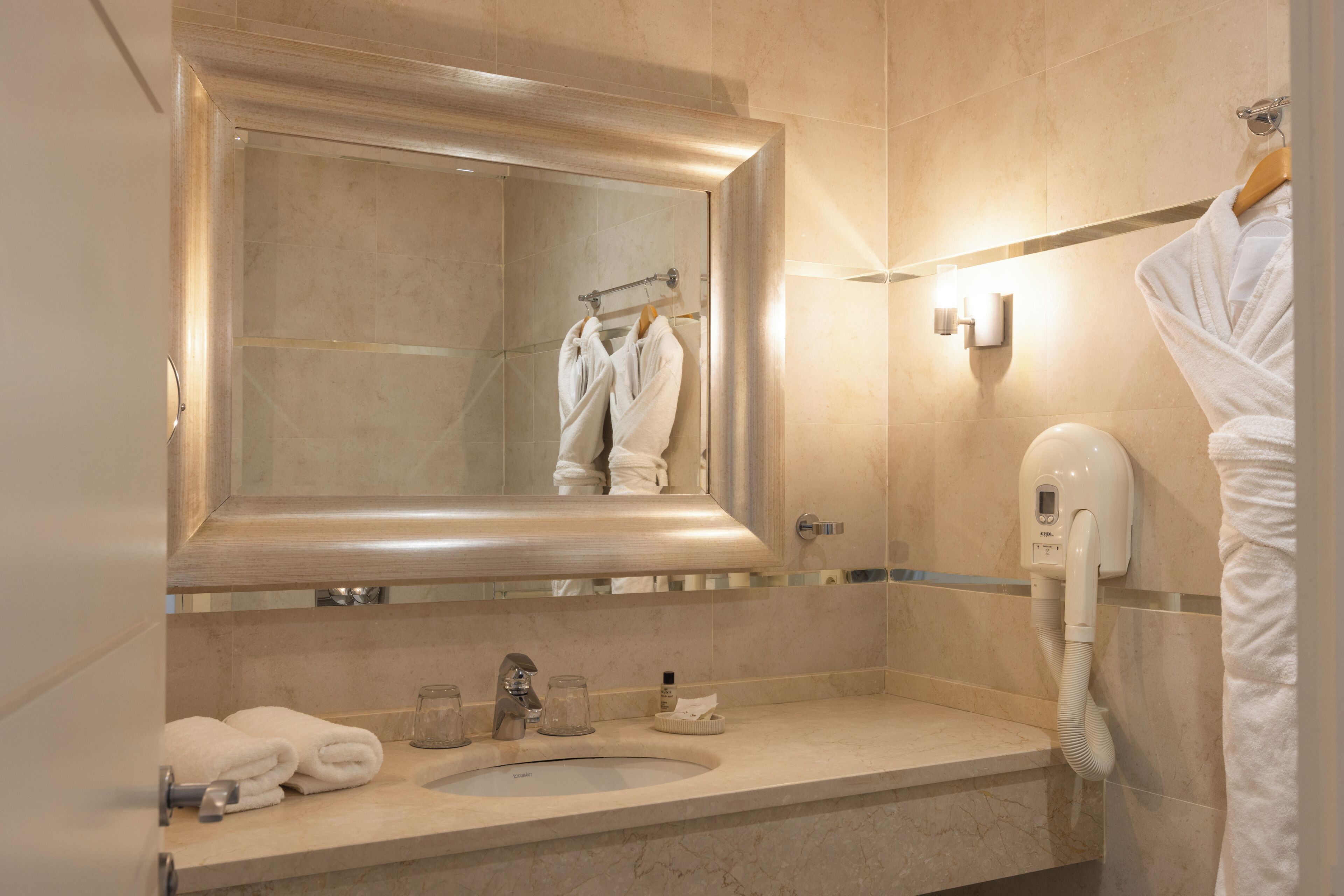A bathroom with a large mirror, a sink, a towel rack, and a hairdryer.