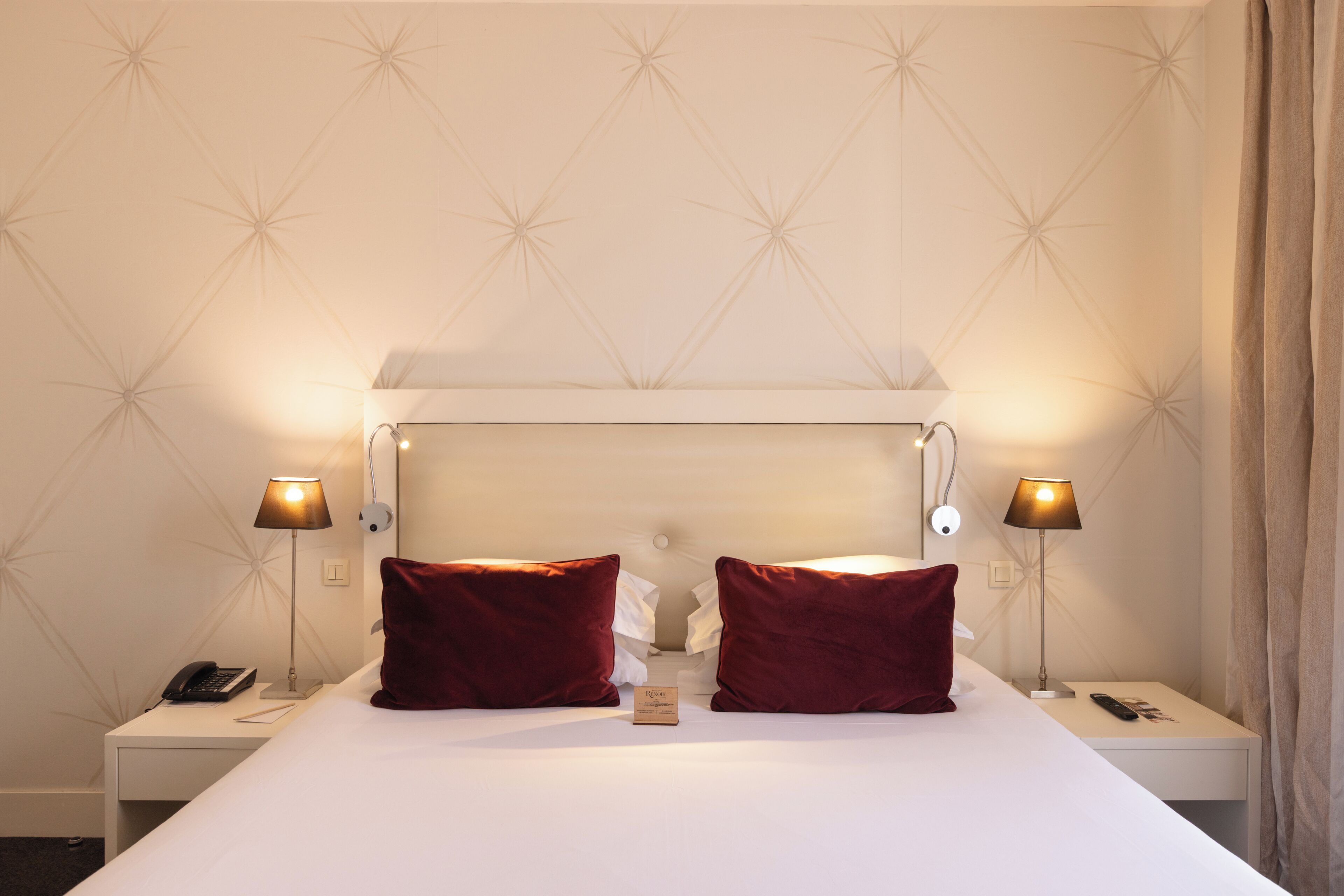 Une chambre d’hôtel avec un grand lit, deux lampes de chevet, une table de chevet avec un téléphone et un mur orné d’un motif géométrique.