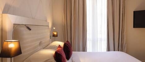 A hotel room with a bed, a lamp, a TV, and a window with curtains.