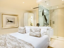 Een moderne hotelkamer met een groot bed, een douchecabine van glas en een ingelijst kunstwerk aan de muur.