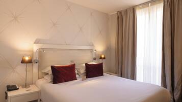 A hotel room with a bed, two bedside lamps, a nightstand, and a window with curtains.