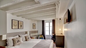 A hotel room with a large bed, a desk, a chair, a TV mounted on the wall, and framed pictures on the wall. - Hôtel Sèvres Saint Germain (Paris)