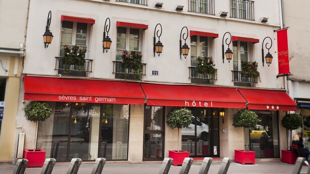 A hotel with a red awning, multiple balconies, and outdoor seating. - Hôtel Sèvres Saint Germain (Paris)