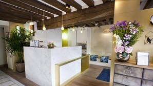 A reception area with a marble counter, wooden beams, hanging light fixtures, a potted plant, and a vase of flowers. - Hôtel Sèvres Saint Germain (Paris)