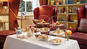 A room with a table set for tea service, a bookshelf, and a red armchair. -  Macdonald Craxton Wood Hotel & Spa, Chester (Ellesmere Port)