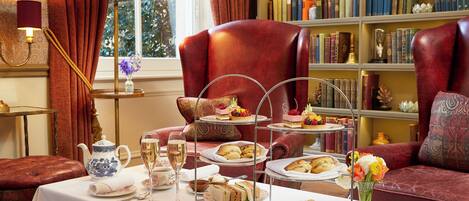 A room with a table set for tea service, a bookshelf, and a red armchair.