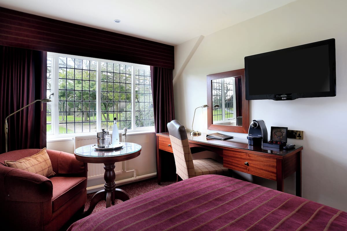 A hotel room with a bed, a desk, a chair, a TV, and a window with curtains.