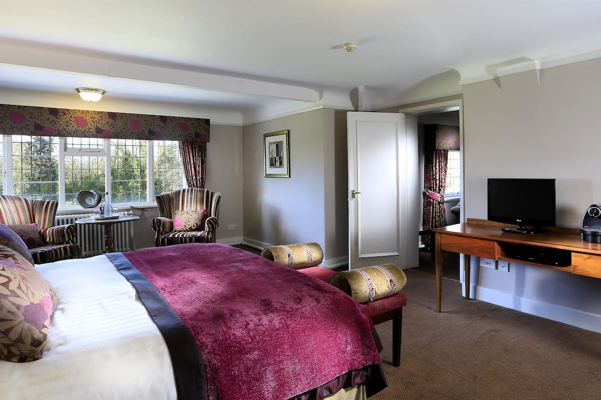A hotel room with a large bed, a desk with a television, a chair, and a window with curtains.